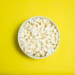 A white bowl full of tasty popcorn on a bright yellow background, perfect for snacks or movie nights.