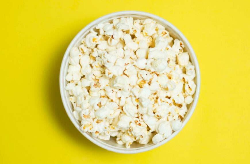 A white bowl full of tasty popcorn on a bright yellow background, perfect for snacks or movie nights.